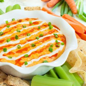 Slow cooker buffalo chicken dip with celery, crackers, carrots and chips