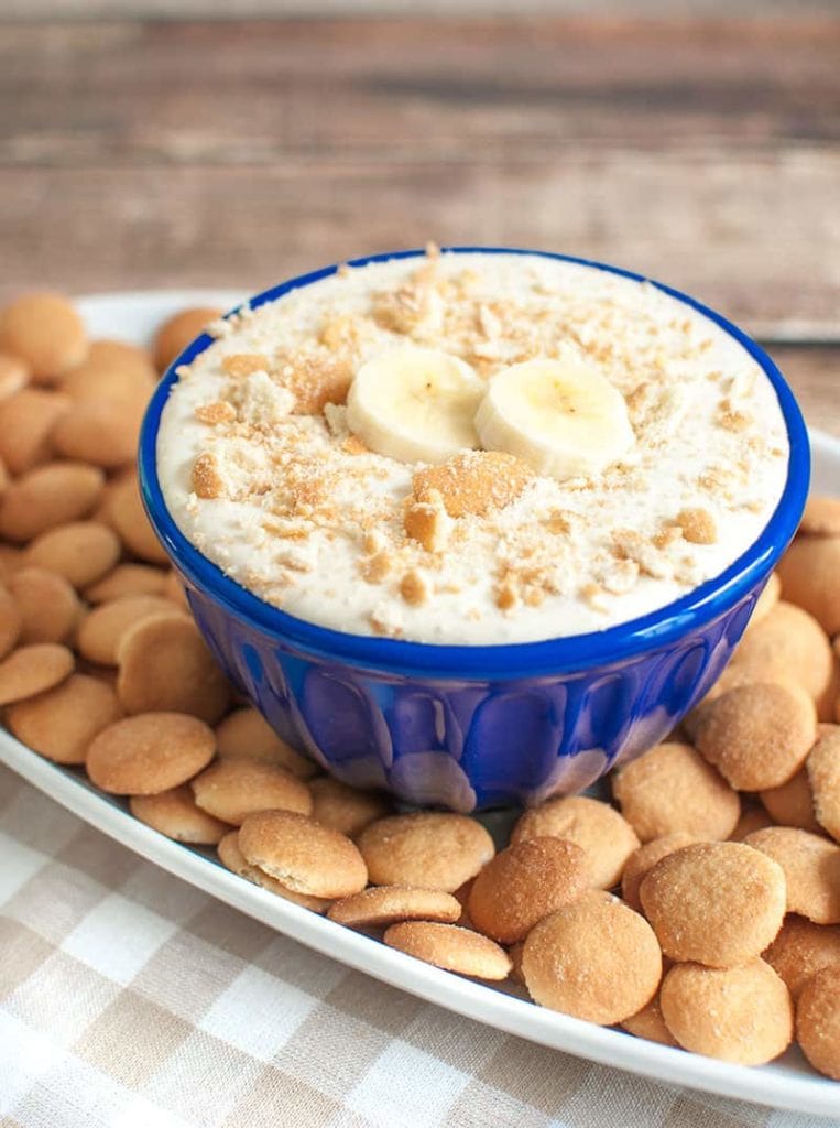 Blue bowl of banana pudding dip topped with vanilla wafer crumbs 