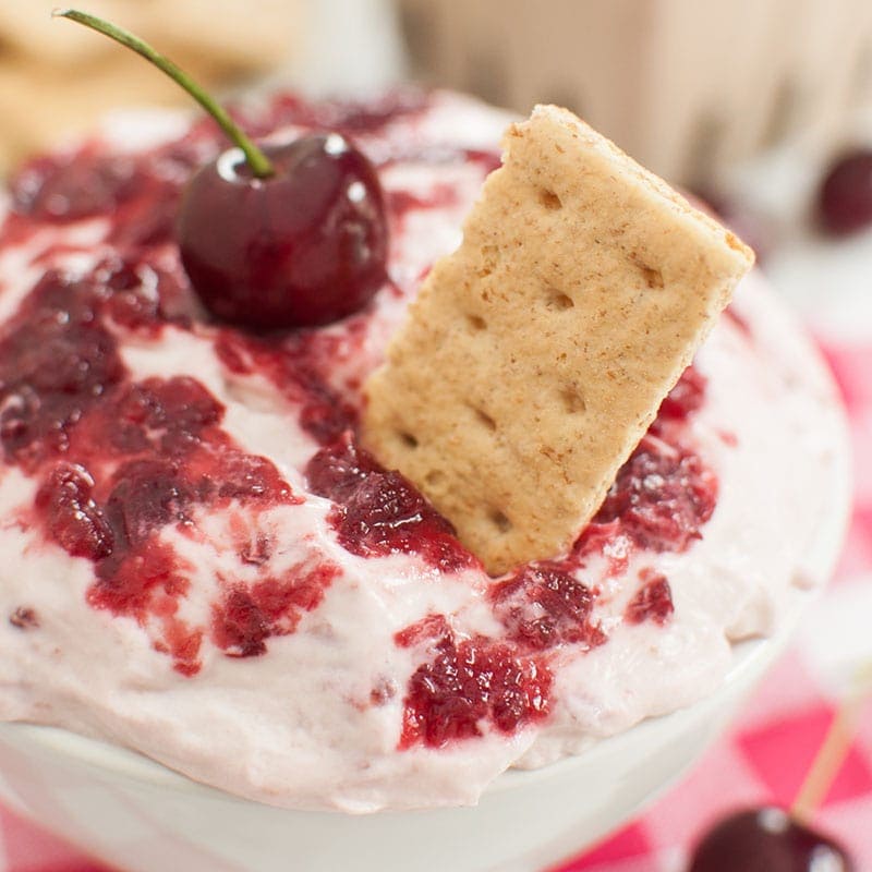 Graham cracker in a bowl of cherry cheesecake dip
