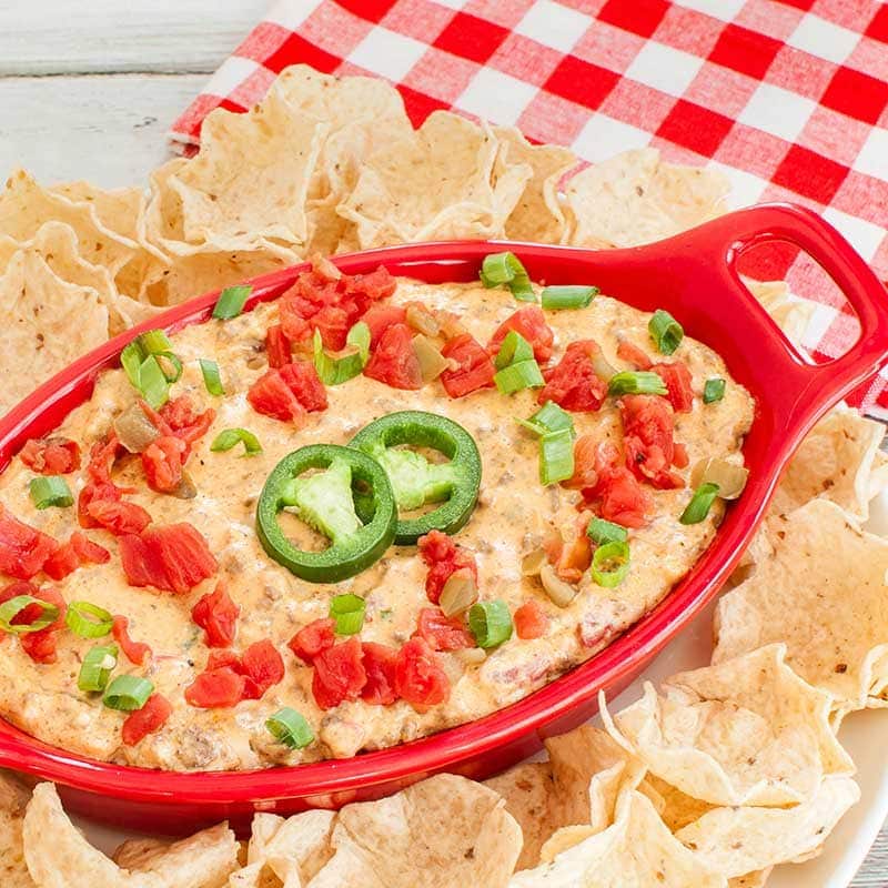 Rotel dip in a red baking dish topped with more rotel, green onions and jalapeno slices