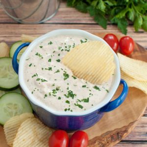 bowl of sour cream dip on a serving board with chips and veggies