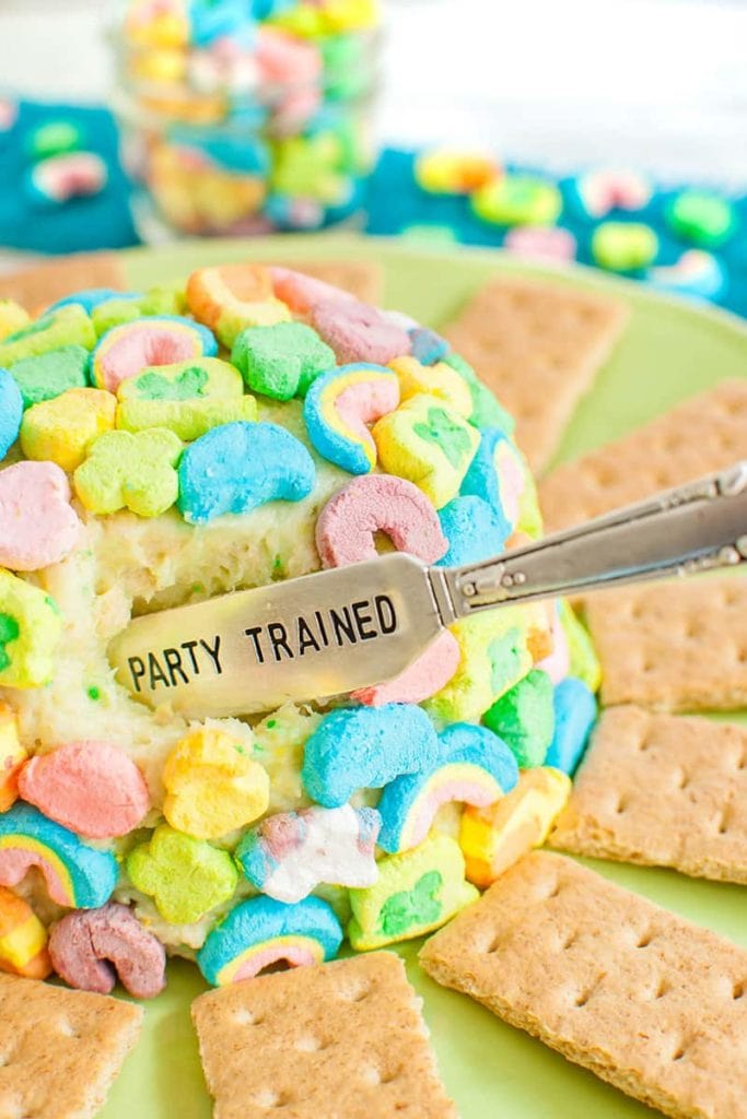 bite cut out of a lucky charms cheesecake cheese ball with spreader that reads party trained