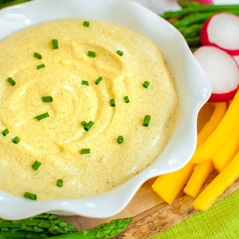 yellow curry dip topped with chives on a board with veggies