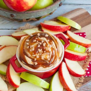 red bowl of caramel dip surrounded by apple slices