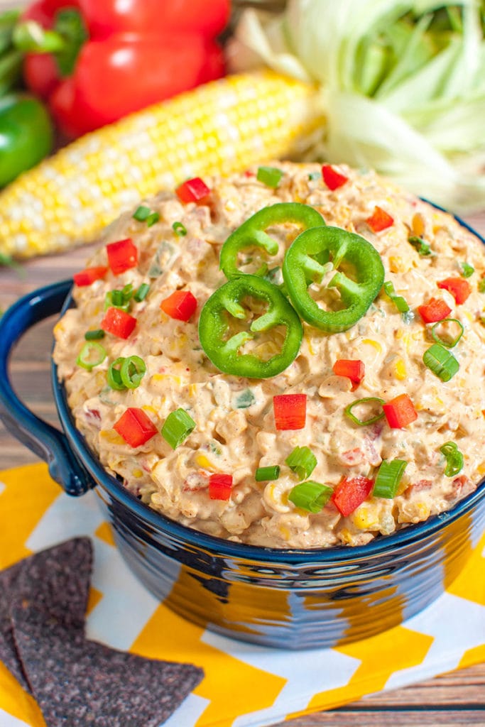 blue bowl of mexican corn dip topped with sliced jalapenos
