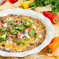 black bean dip in a white dish topped with melted cheese and jalapenos