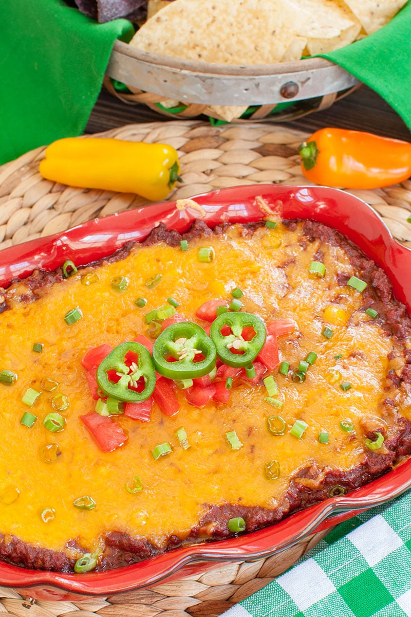 red baking dish of cheesy dip topped with tomatoes and jalapenos