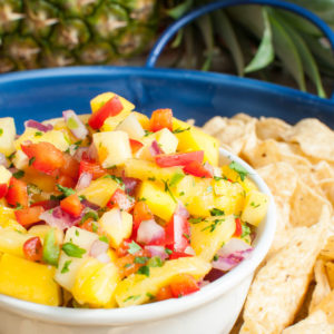 pineapple mango salsa in a white bowl on a blue platter with cips