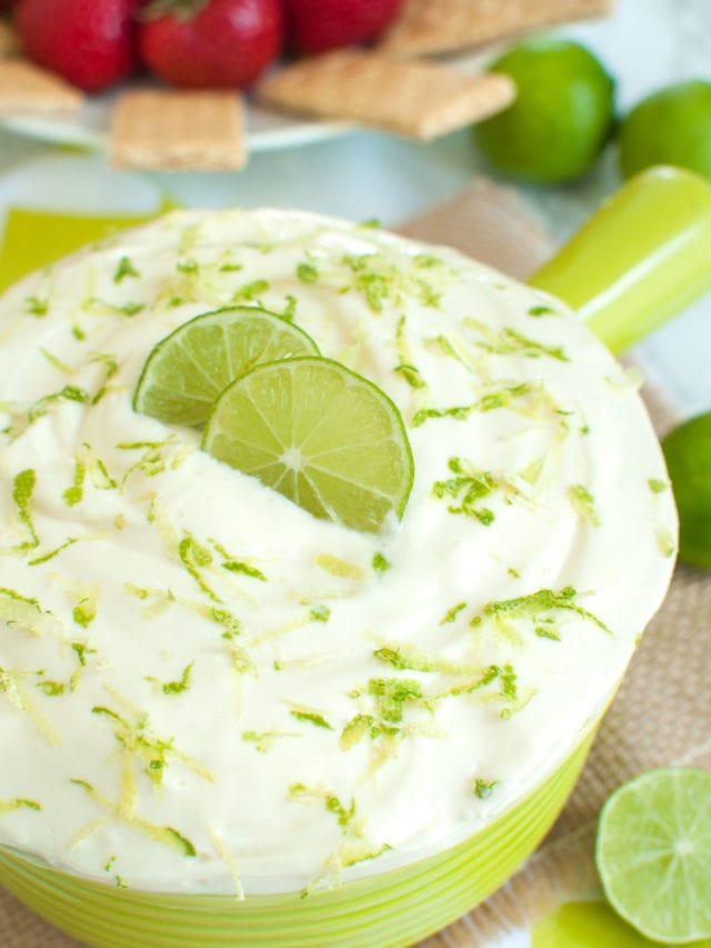 green bowl of dip topped with lime slices and zest and surrounded by limes