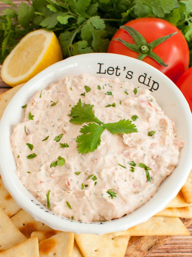 white bowl of dip surrounded by a half lemon, tomato and cilantro