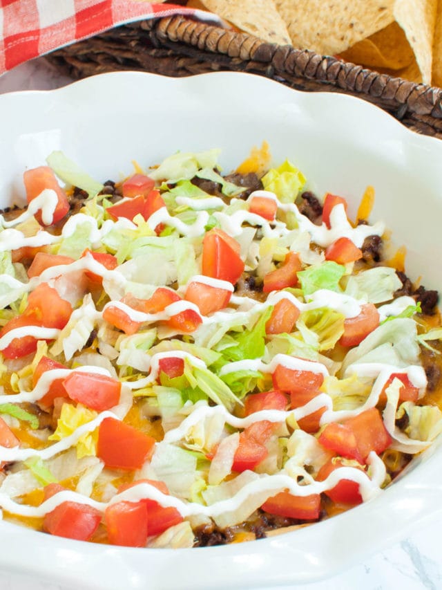 white pie dish of dip topped with lettuce, tomatoes and sour cream