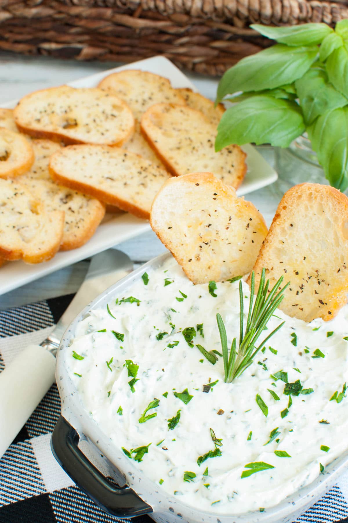 crostini dipped into a square dish of whipped goat cheese dip topped with herbs