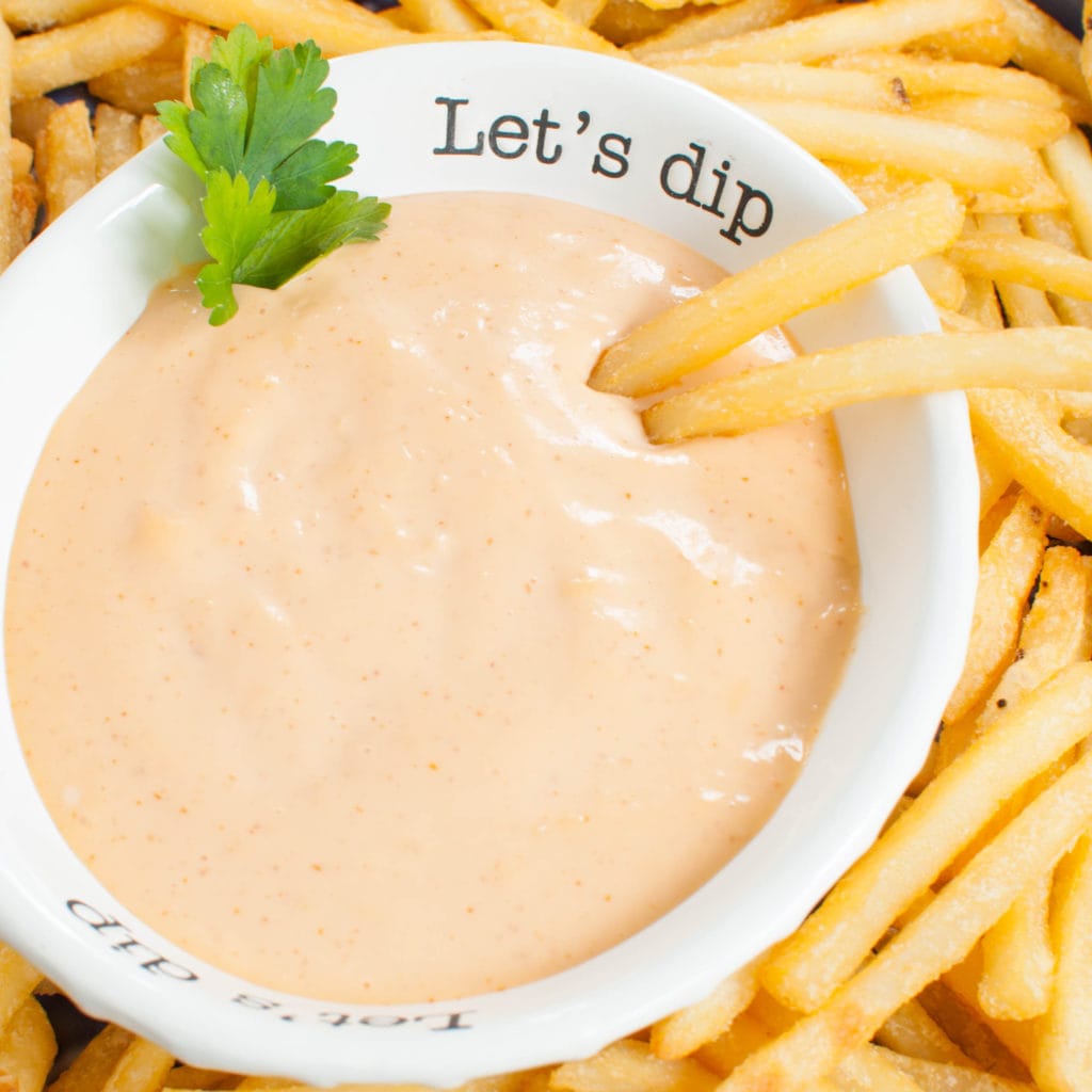 2 french fries dipped into a bowl of sriracha aioli